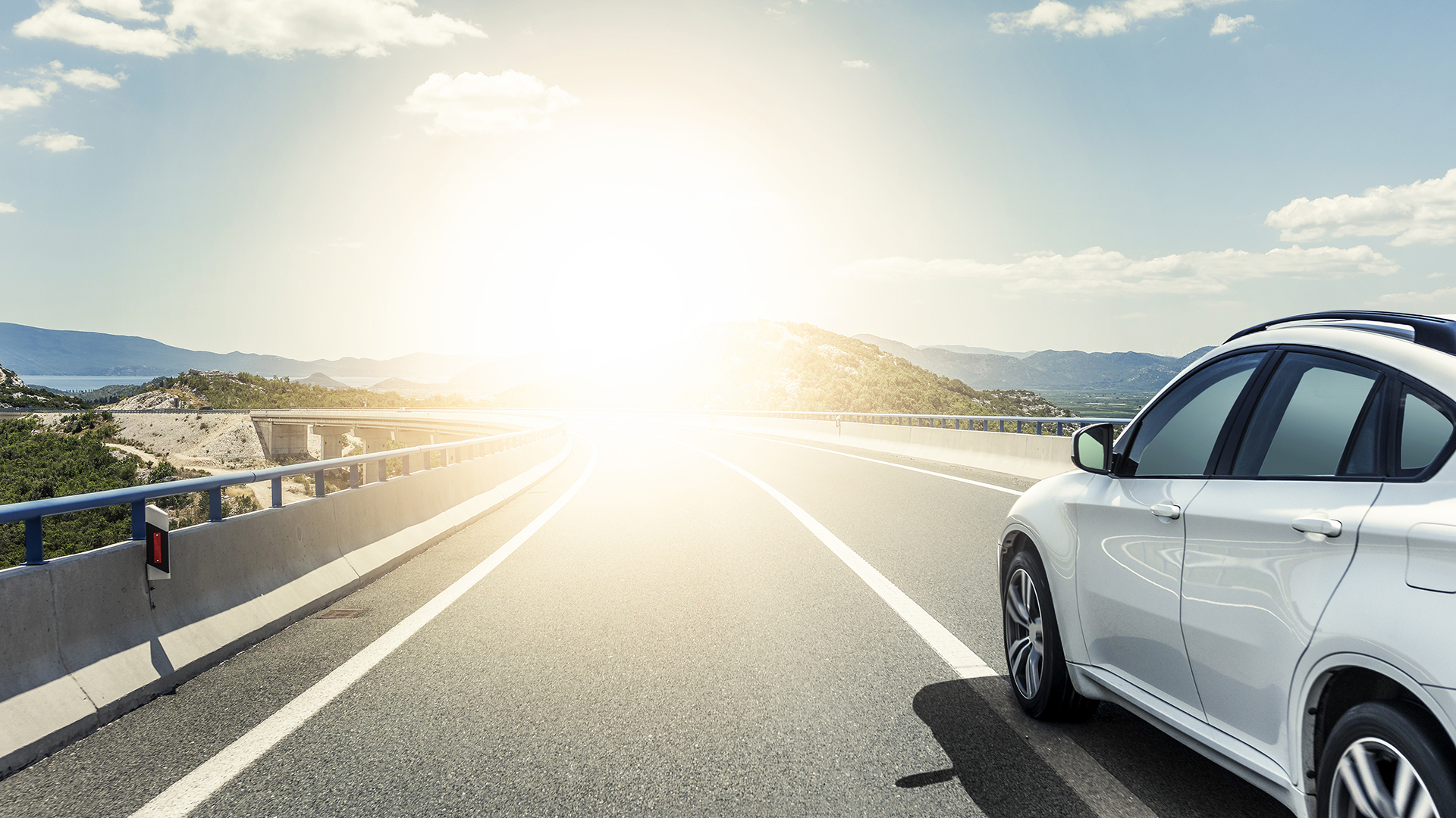A White Car Rushing Along A High Speed Highway In The Sun.